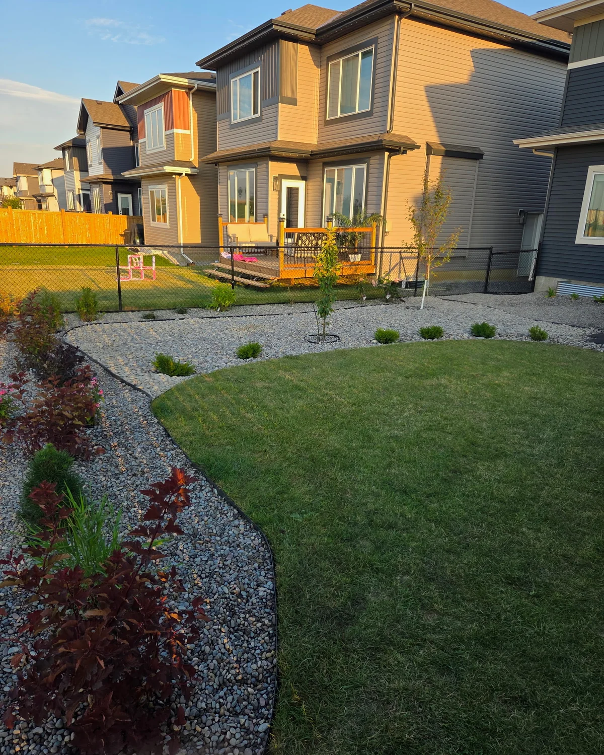 Full-property landscape installation with curved decorative rock beds, lawn, trees and shrubs
